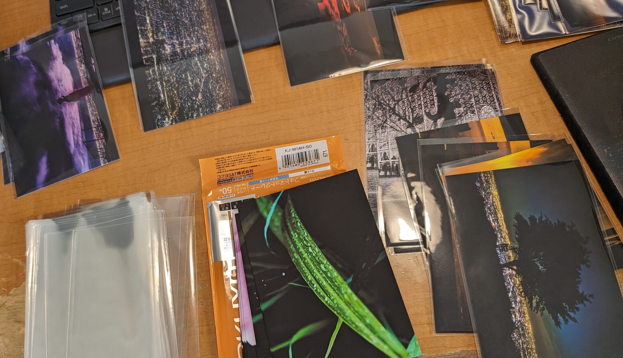 Image of this image features a tabletop display of various photographs laid out for sorting or organizing. the pictures showcase diverse themes, including cityscapes, nighttime landscapes, and nature. a packet of clear protective sleeves is visible, suggesting an archival or collection setup. the