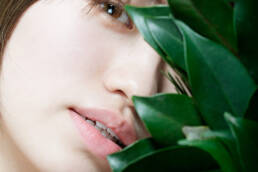 The featured image is a close-up portrait of a young woman partially obscured by green leaves. The photograph captures the subtle details of her face and the natural elements, creating a striking composition.