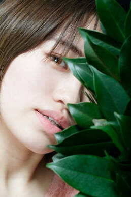 The featured image is a close-up portrait of a young woman partially obscured by green leaves. The photograph captures the subtle details of her face and the natural elements, creating a striking composition.