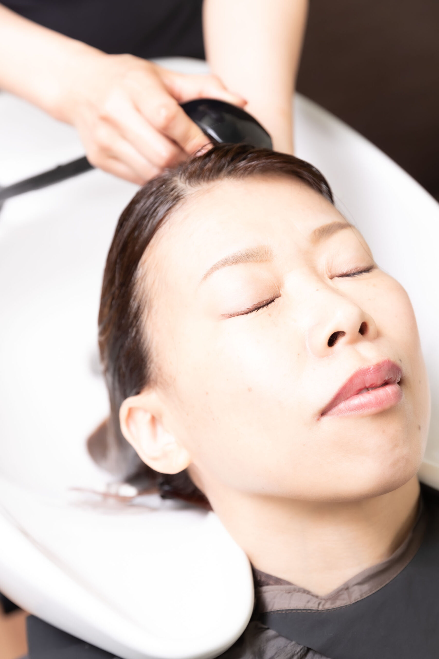 Image of a relaxing salon experience: close-up of a woman enjoying a comforting hair wash at a modern salon. the image captures the soothing ambiance of professional hair treatment, showcasing hair care, beauty services, and relaxation. perfect for depicting luxury spa treatments, haird