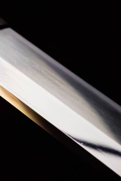 Image of close-up of a traditional japanese katana blade, showcasing its sharp, polished edge against a dark background. the high-quality craftsmanship of the sword is evident in its sleek, reflective surface, highlighting its cultural significance in martial arts and japanese history.