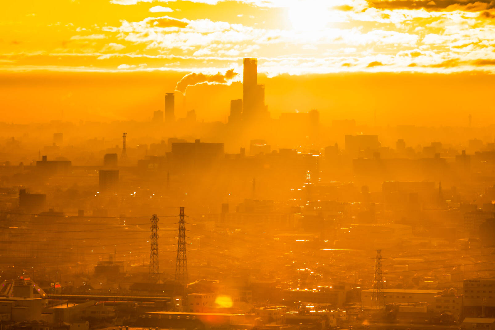 Image of the image depicts a cityscape at sunset, bathed in a warm orange glow. the skyline is dotted with tall buildings, industrial smokestacks, and power lines, creating a silhouette against the vibrant sky. the urban scene highlights the essence of city