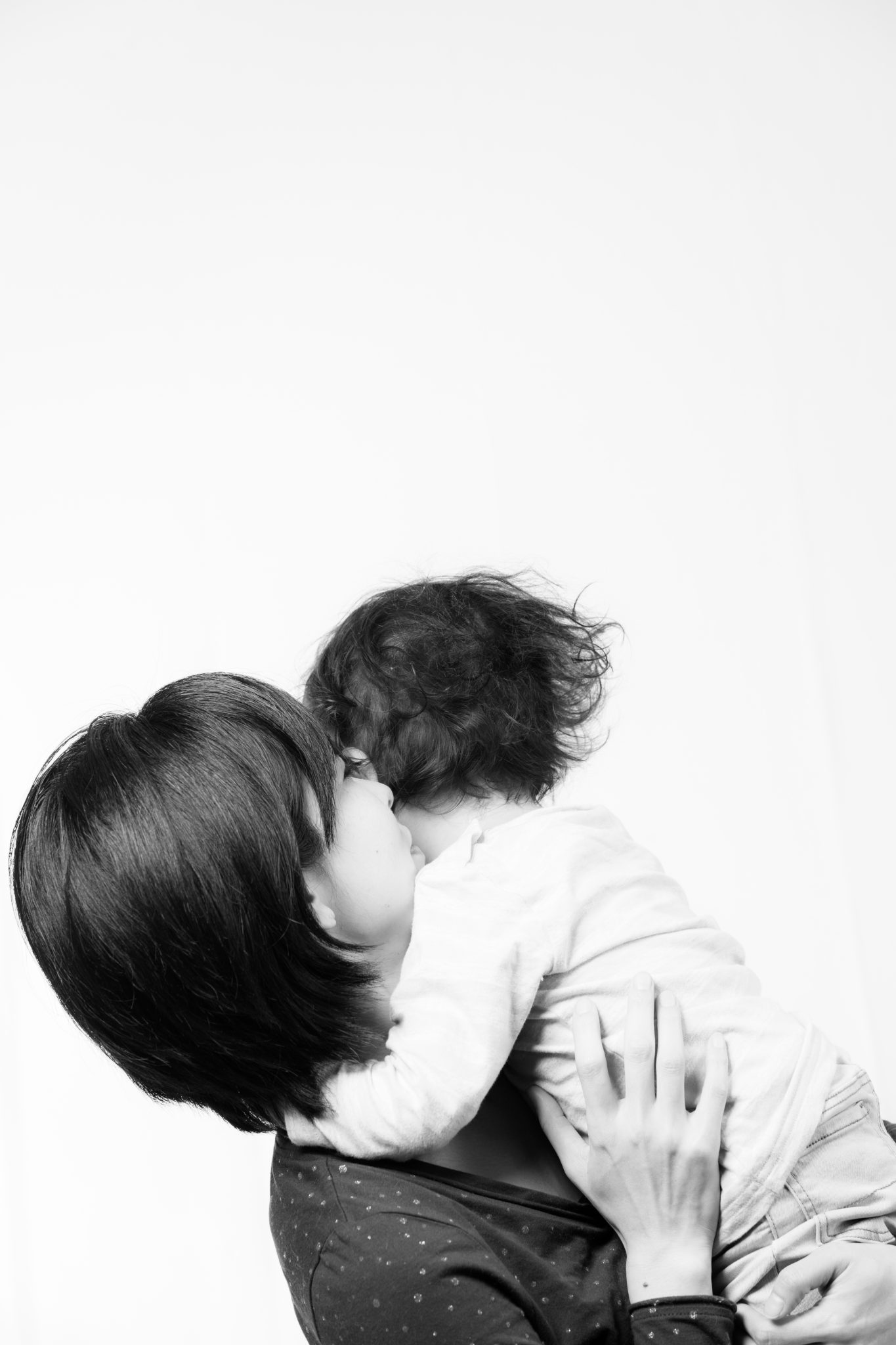 Image of a black and white portrait captures a tender moment between a woman and her child, highlighting love and connection. the woman embraces the child closely, showcasing a strong maternal bond. the minimalist background emphasizes the emotional focus, creating a heartwarming family scene. keywords