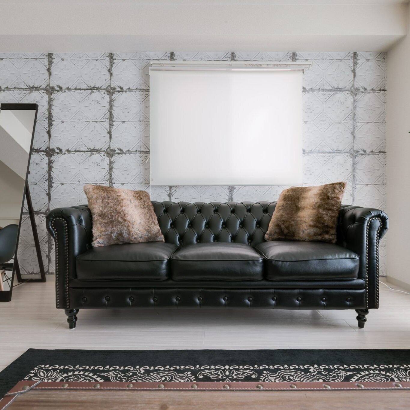 Image of modern living room featuring a luxurious black leather tufted sofa with plush brown pillows. the space is enhanced by a stylish patterned wallpaper and a tall, sleek mirror. a green potted plant adds a touch of nature, while a decorative rug complements the contemporary