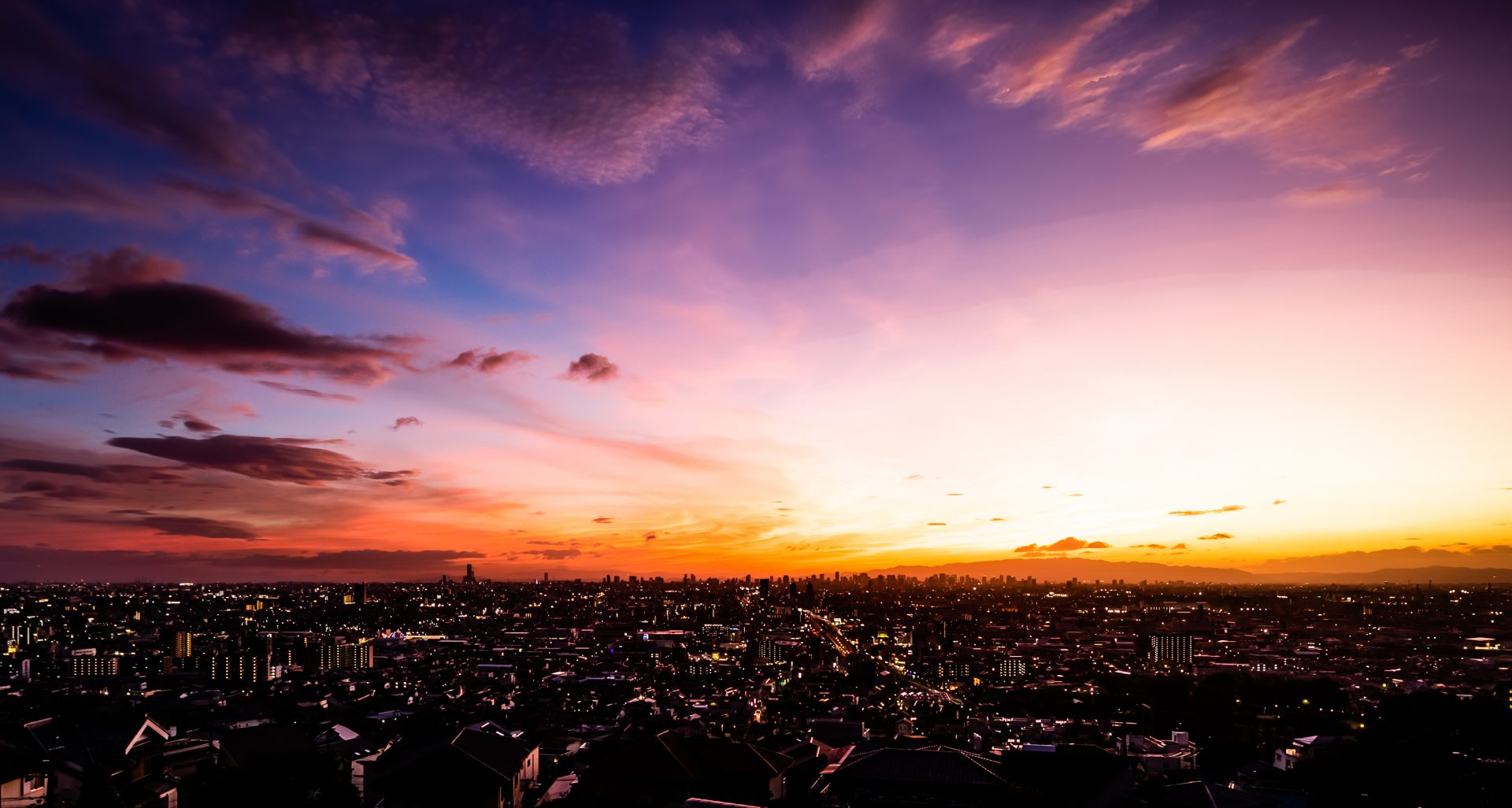 Image of this image captures a breathtaking urban sunset over a bustling cityscape, showcasing vibrant colors of orange, purple, and pink sky hues. the distant city skyline is illuminated, creating a stunning contrast against the twilight backdrop. perfect for cityscape, sunset photography,