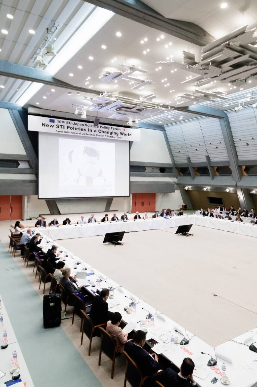Image of the image showcases the 10th eu-japan scientific policy forum held at the kyoto international conference center. the spacious conference room features a large round table with numerous international delegates engaged in discussions. the event focuses on 