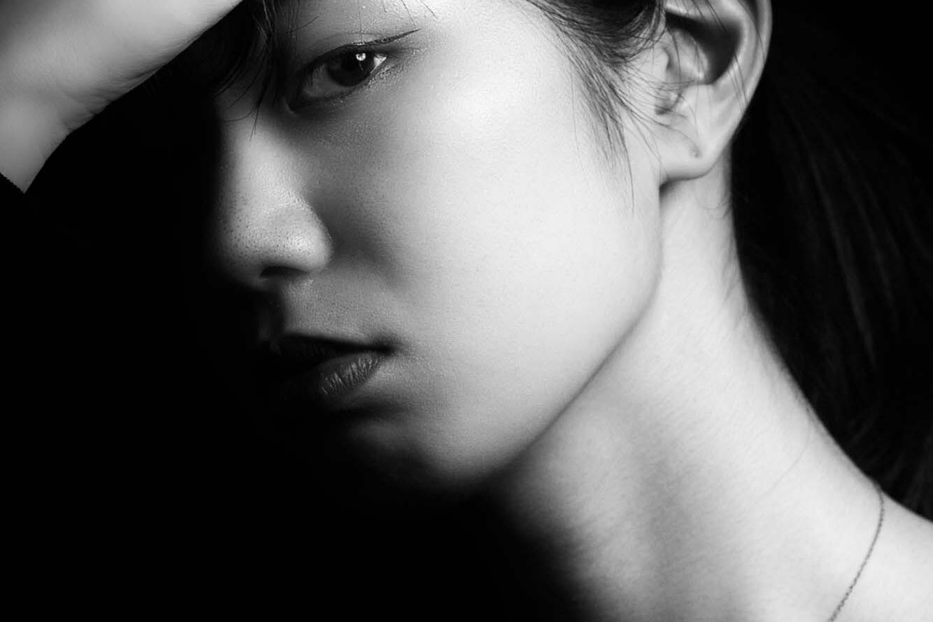 Image of this captivating black-and-white portrait captures a pensive moment as a woman holds her head with her hand. the dramatic lighting and shadows emphasize the introspective mood and elegance, while the minimalist composition highlights the beauty and emotion of the scene. perfect for themes