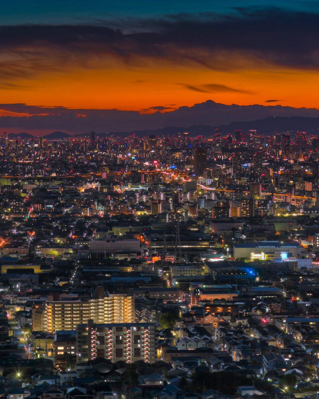 Image of cityscape at dusk featuring a vibrant urban skyline with twinkling city lights under an orange and blue sunset sky. this panoramic view captures the lively atmosphere of a bustling metropolis, highlighting the contrast between natural twilight and artificial illumination. ideal for keywords like city
