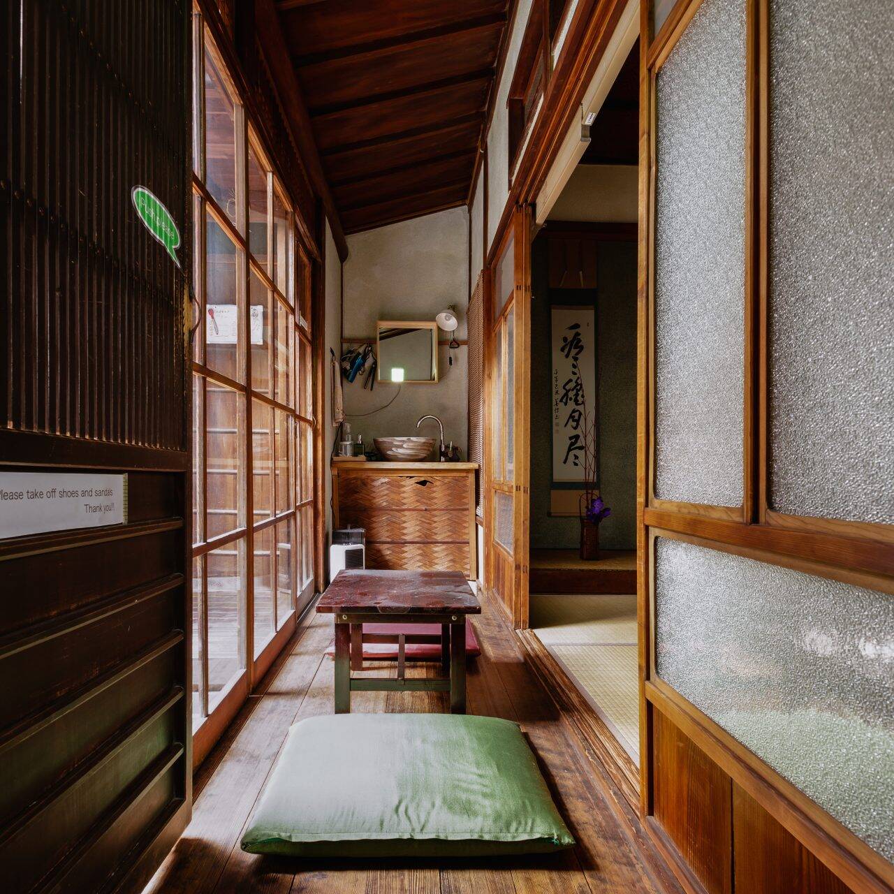 Image of this image showcases the interior of a traditional japanese home with wooden flooring and sliding shoji doors. the narrow hallway features a small wooden table and green cushions for seating, evoking a serene and minimalist ambiance. the space is beautifully lit, highlighting the wooden