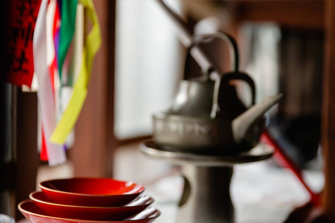 Image of this image captures a serene japanese setting featuring a stack of vibrant red lacquer bowls and a traditional kettle on a shelf. colorful ribbons and a japanese banner add cultural significance to the scene, which is set against a softly lit wooden interior. ideal for keywords