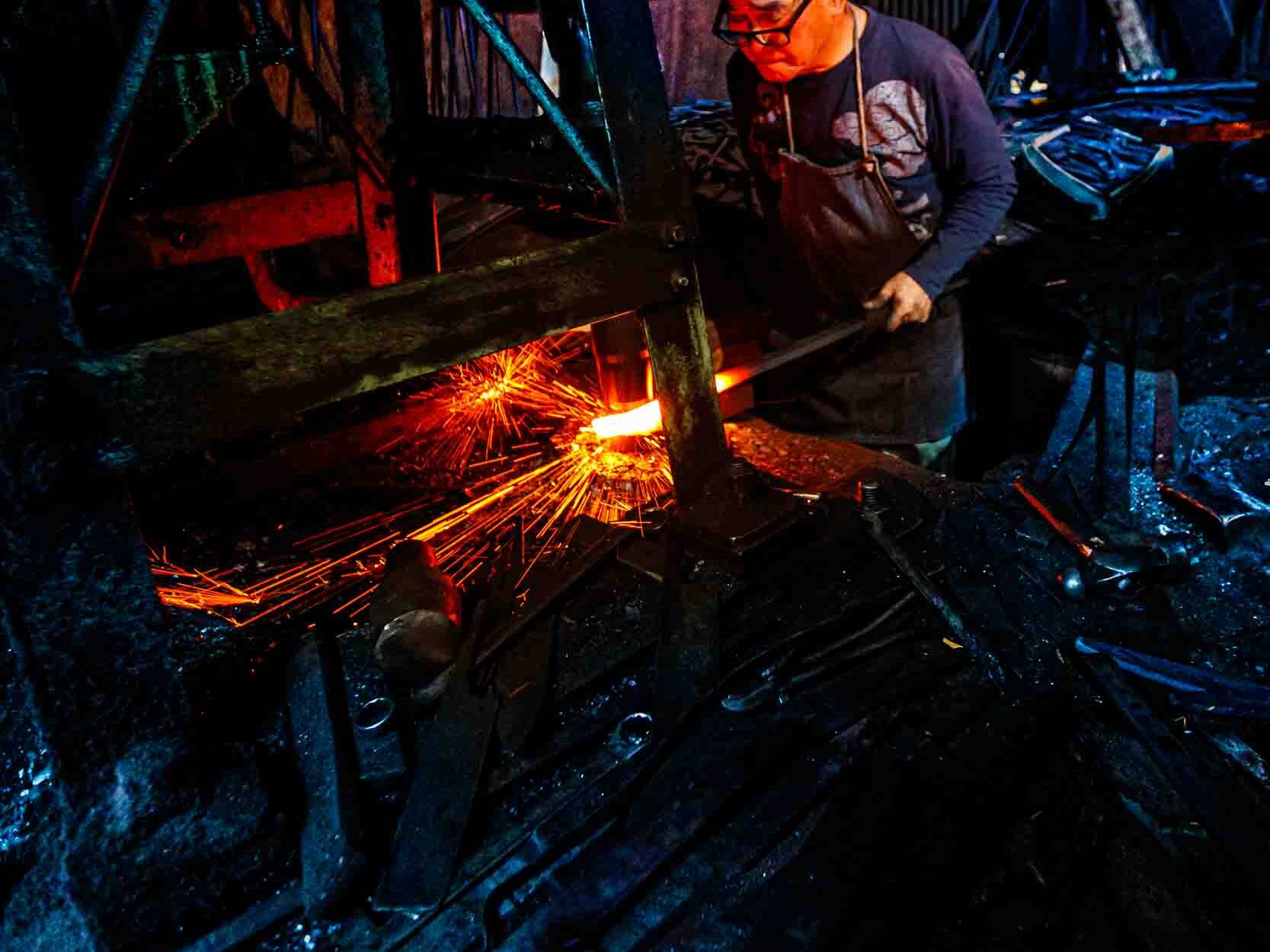 Image of a blacksmith working in a dimly lit forge, surrounded by sparks flying from heated metal. this industrial setting showcases traditional craftsmanship, with the artisan intensely focused on shaping the glowing iron. a perfect representation of skilled metalwork, the scene highlights the dramatic