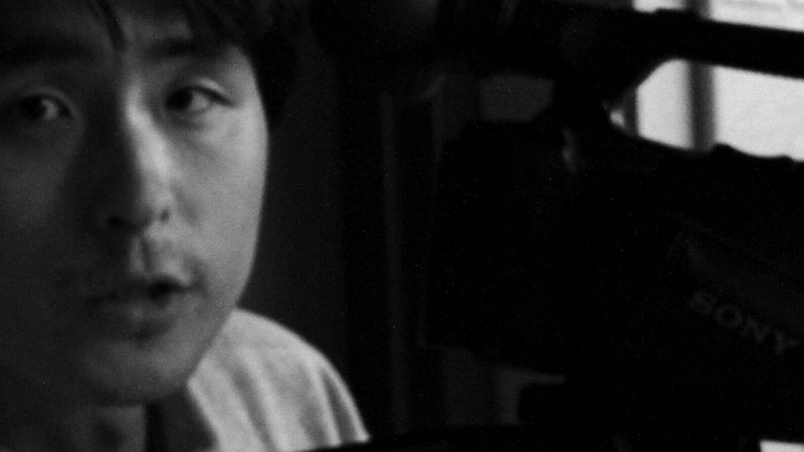 Image of a black-and-white photograph shows a person near a video camera. the image captures a close-up of the person's face, while the camera is partially visible. the composition and grayscale tones create an artistic, vintage feel, ideal for content related to photography,