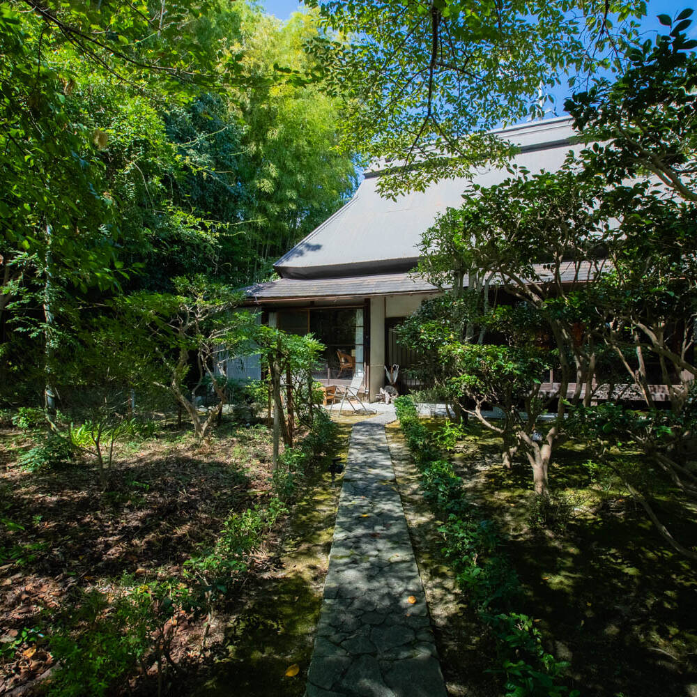 Image of serene japanese garden with lush greenery and a traditional house, showcasing a stone path leading through a tranquil yard. this idyllic scene is perfect for those seeking peace and nature-inspired architecture.