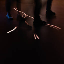 Image of this image features a dimly lit scene with blurred silhouettes of people walking on a dark floor. light streaks create an abstract pattern across the ground, enhancing the mysterious atmosphere. the composition highlights movement and shadow, making it ideal for keywords like abstract photography