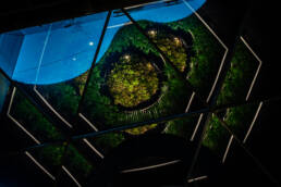 Image of futuristic geometric architecture and lush greenery create a modern, eco-friendly design seen through a glass ceiling. the vibrant green plant installations and reflective surfaces offer a stunning visual contrast to the sleek lines and glowing lights, embodying sustainability in architectural innovation. perfect