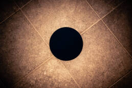 Image of this image features a black circle centered on a textured brown tiled floor. the tiles are arranged in a diagonal pattern, creating a geometric aesthetic that highlights the contrast between the dark circle and the lighter background. keywords: black circle, textured tiles, geometric pattern