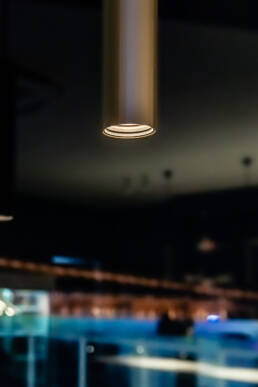Image of a modern, cylindrical pendant light fixture illuminated in a dimly lit room, creating a cozy ambiance. the soft, focused light contrasts with the dark, blurred background, highlighting the fixture's sleek design. ideal for interior design keywords such as 