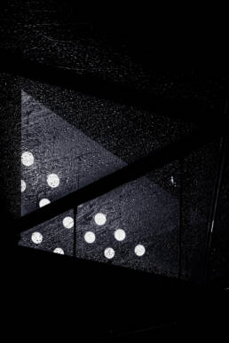 Image of abstract image featuring glowing white circular lights through a rain-soaked glass ceiling. the dark, moody atmosphere highlights raindrops and reflections, creating a captivating urban night scene. keywords: abstract lights, rainy night, glass ceiling, urban atmosphere.