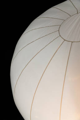 Image of close-up of a white hot air balloon against a dark sky. the balloon's fabric features distinct seams and a circular pattern. perfect for searches related to hot air balloons, night photography, or aerial adventures.