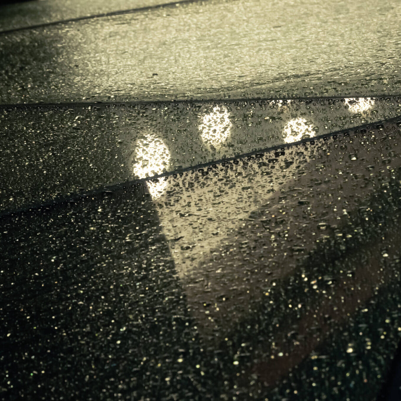 Image of rain-covered glass roof with a geometric design reflecting ambient lights, creating a moody and atmospheric urban scene. perfect for themes related to architecture, weather, and urban photography.