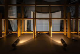 Image of the image showcases a modern architectural interior featuring a minimalist design with wooden frames and strategically placed spotlights casting warm glows. the structured backdrop and sleek lighting create an atmosphere of contemporary elegance, ideal for galleries or modern buildings. keywords: modern architecture, minimalist