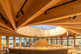 Image of modern wooden interior of a dome-shaped café, featuring sleek architectural design and natural light. the space includes wooden beams, a central bar with taps, and large windows creating an inviting atmosphere. perfect for keywords like 