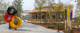 Image of the image showcases the german pavilion at expo 2025 in osaka, japan, featuring a modern architectural design with wooden structures and lush greenery. a colorful sculpture with the words 